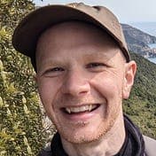 Headshot of Anders Madsen smiling and wearing a cap in nature.